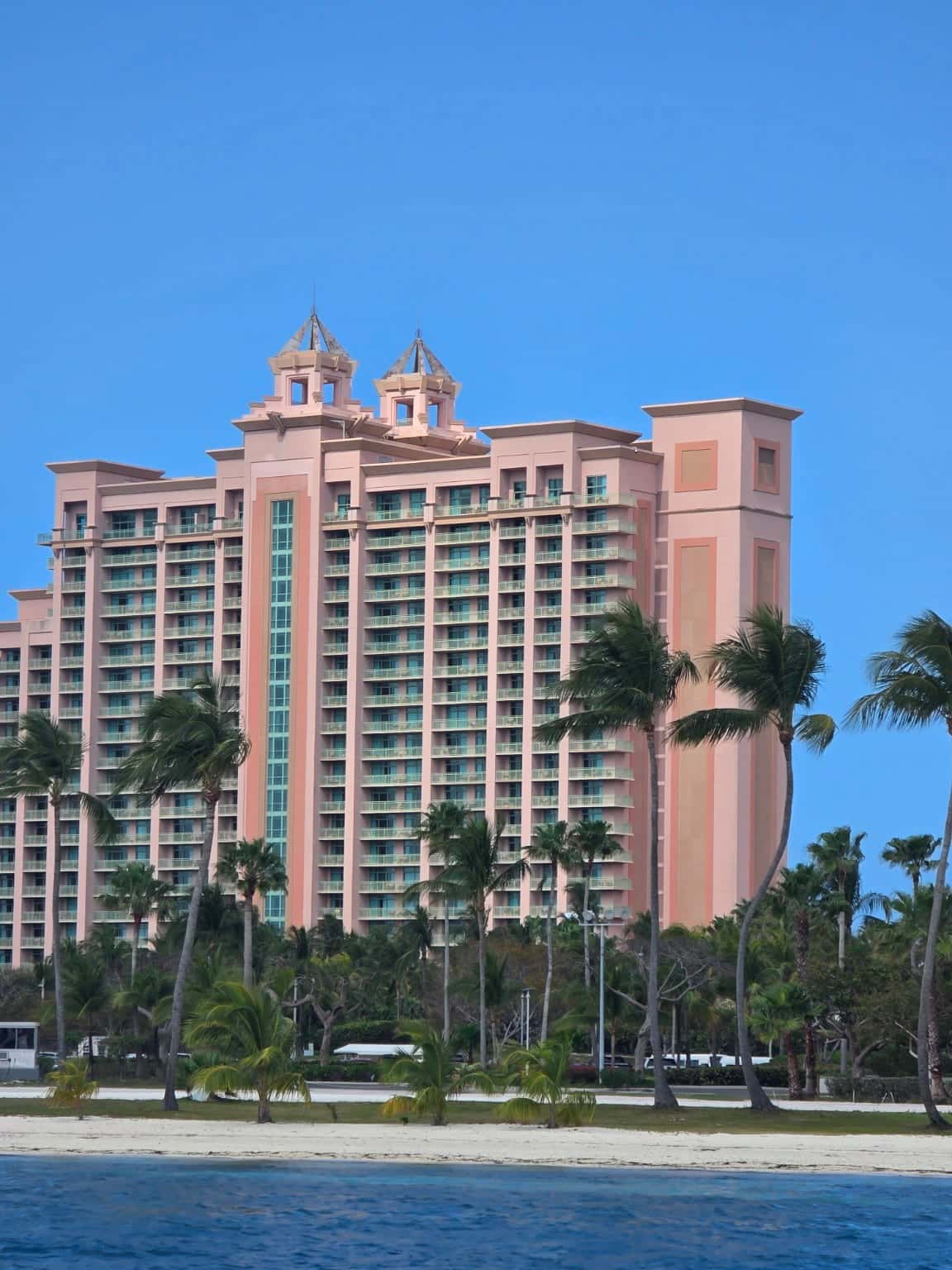 Pink towers and glass balconies of The Reef at Atlantis behind palms and blue water on Paradise Island