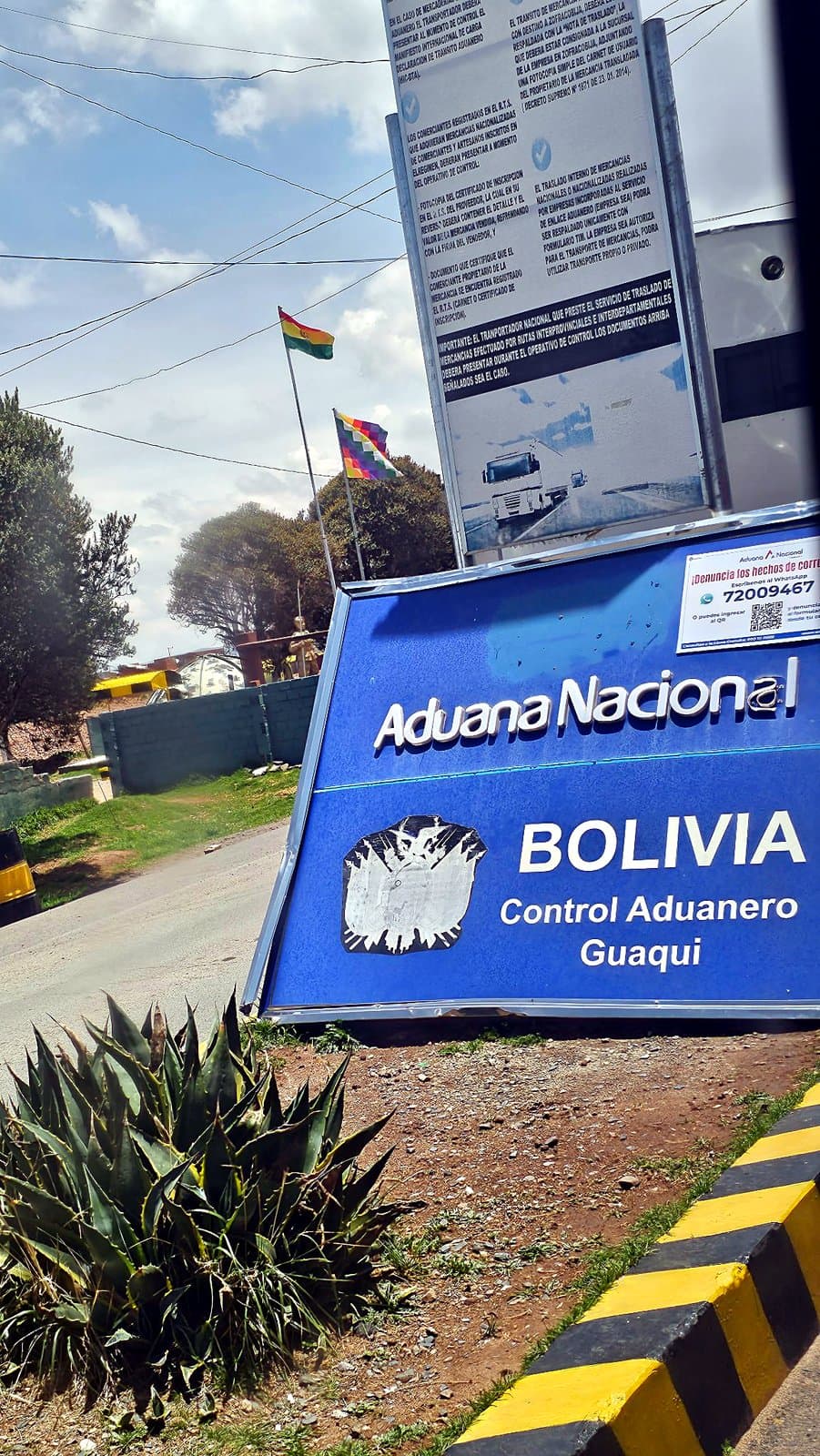 Le panneau bleu de l’Aduana Nacional au contrôle douanier de Guaqui, en Bolivie, avec les drapeaux bolivien et wiphala derrière