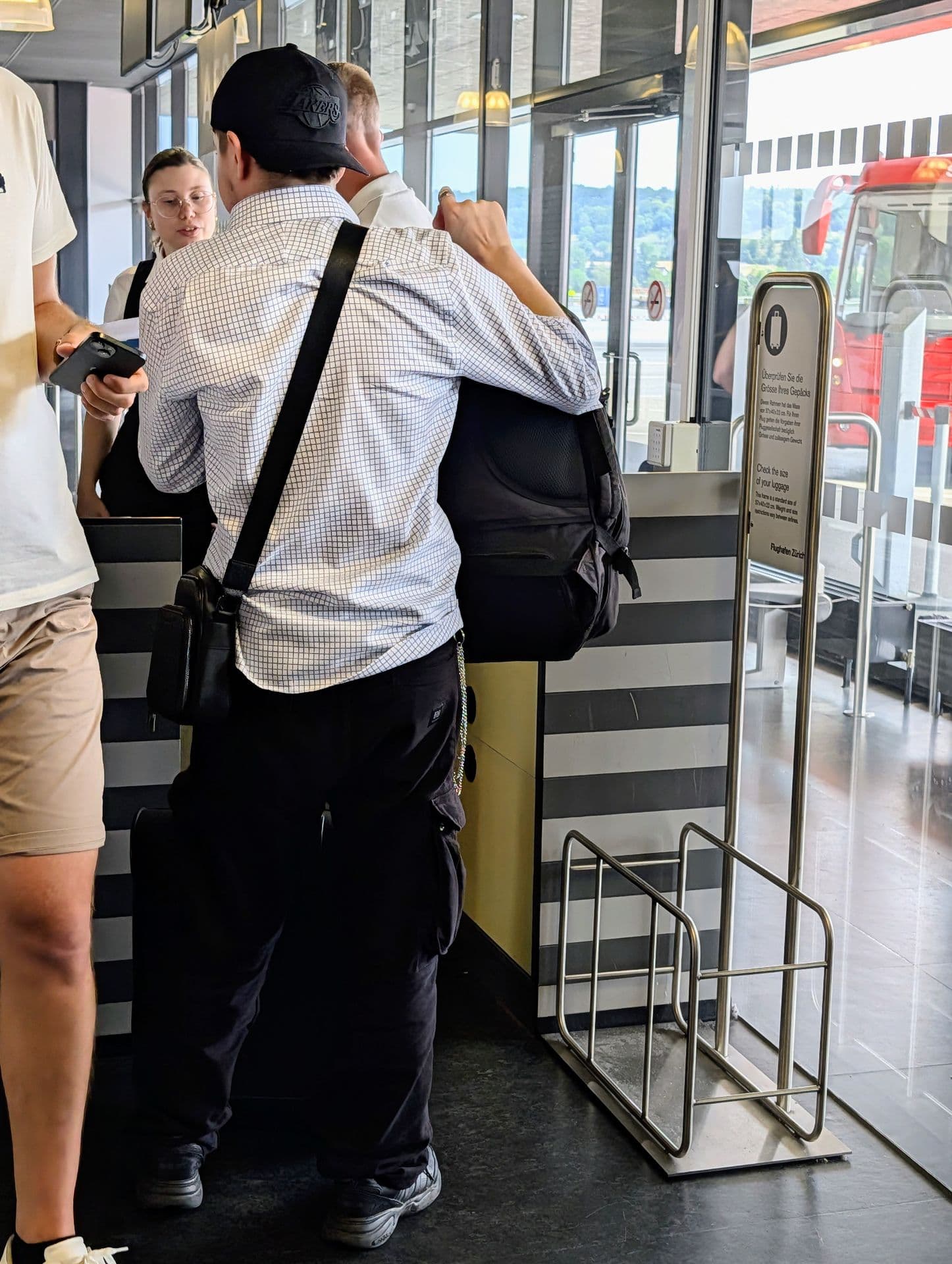 Pasajeros en el mostrador de embarque del aeropuerto de Zúrich, junto a un marco para comprobar el tamaño del equipaje de mano