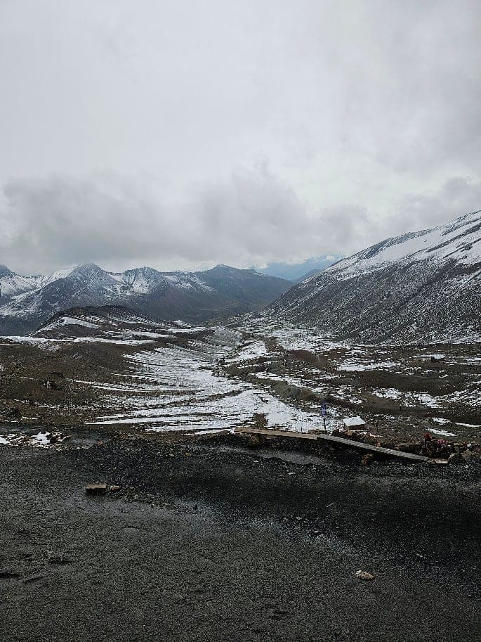 Une haute vallée andine saupoudrée de neige, traversée par un sentier sous de lourds nuages gris