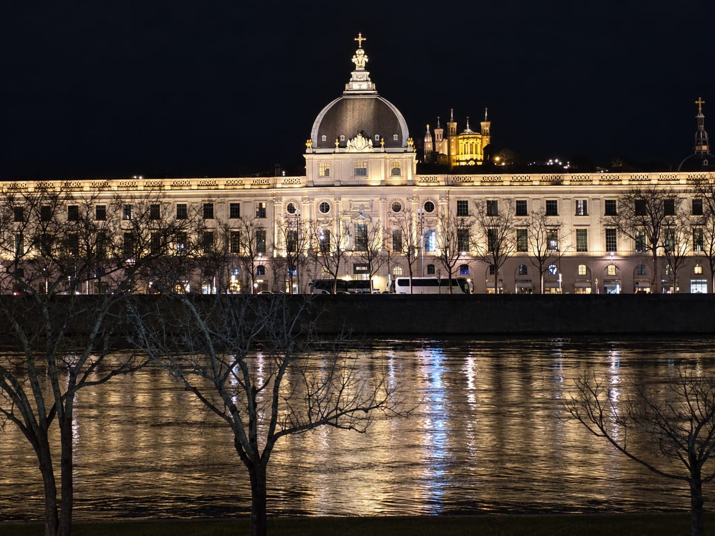 Cúpula y fachada iluminadas del Grand Hôtel-Dieu de Lyon reflejadas en el Ródano por la noche