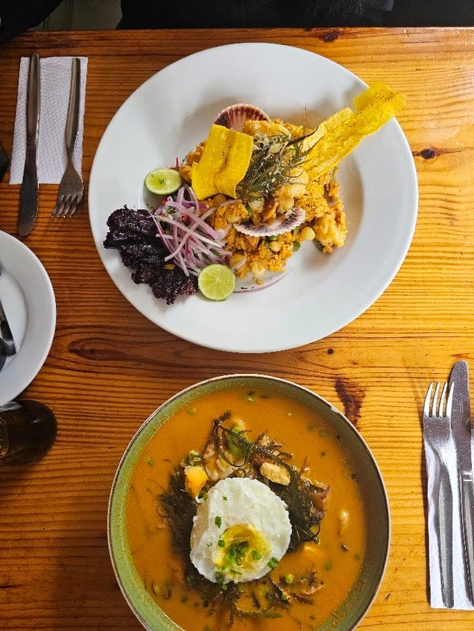 Sur une table de bois, un plat de riz aux fruits de mer garni de croustilles de plantain et de lime, à côté d’une soupe jaune aux fruits de mer avec un œuf au plat